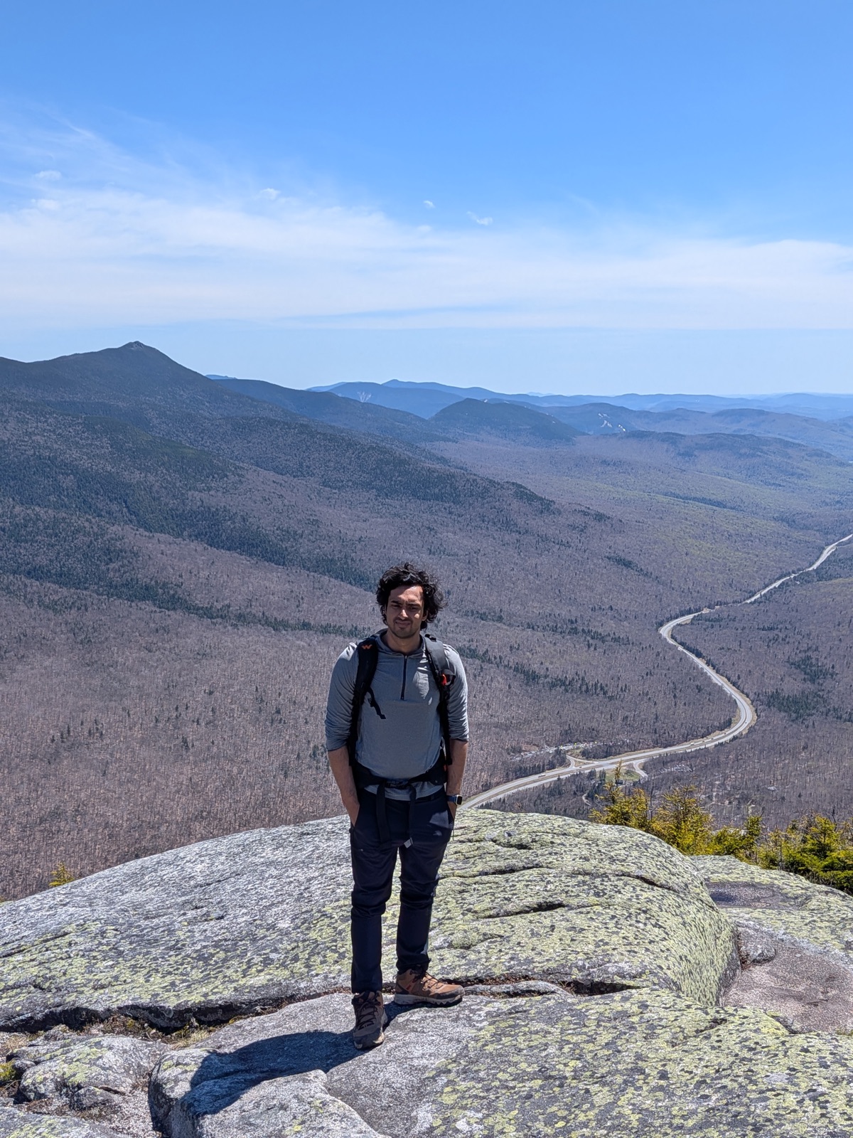 Hiker on a ledge with a highway winding through the valley below