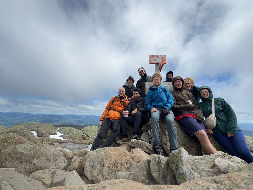 Group of hikers posing on a rocky summit beside the summit sign