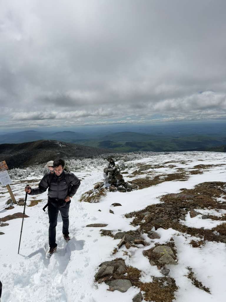 Hiker crossing a snowy alpine plateau next to a cairn