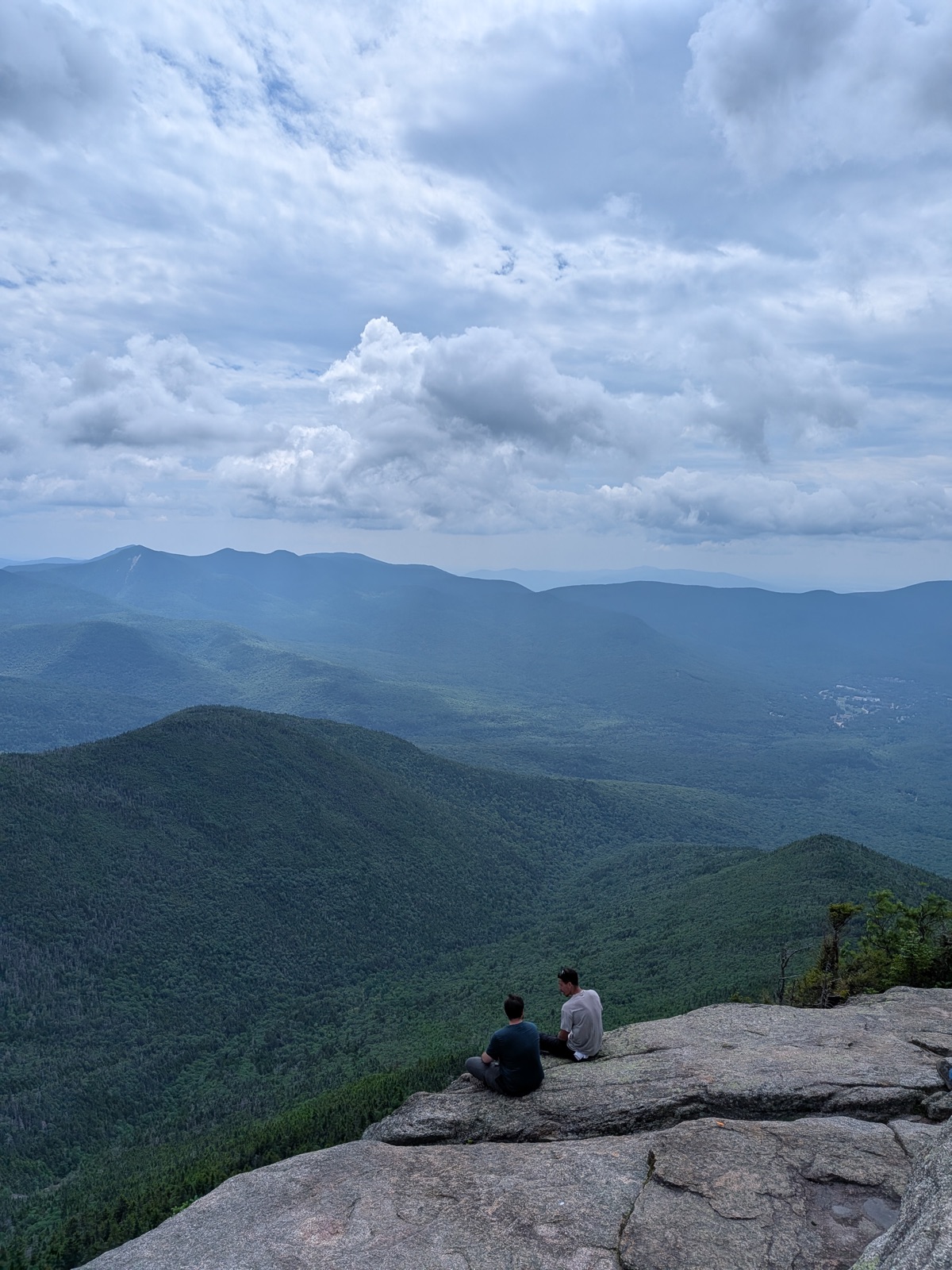 Two hikers sitting on a wide granite ledge above a green valley