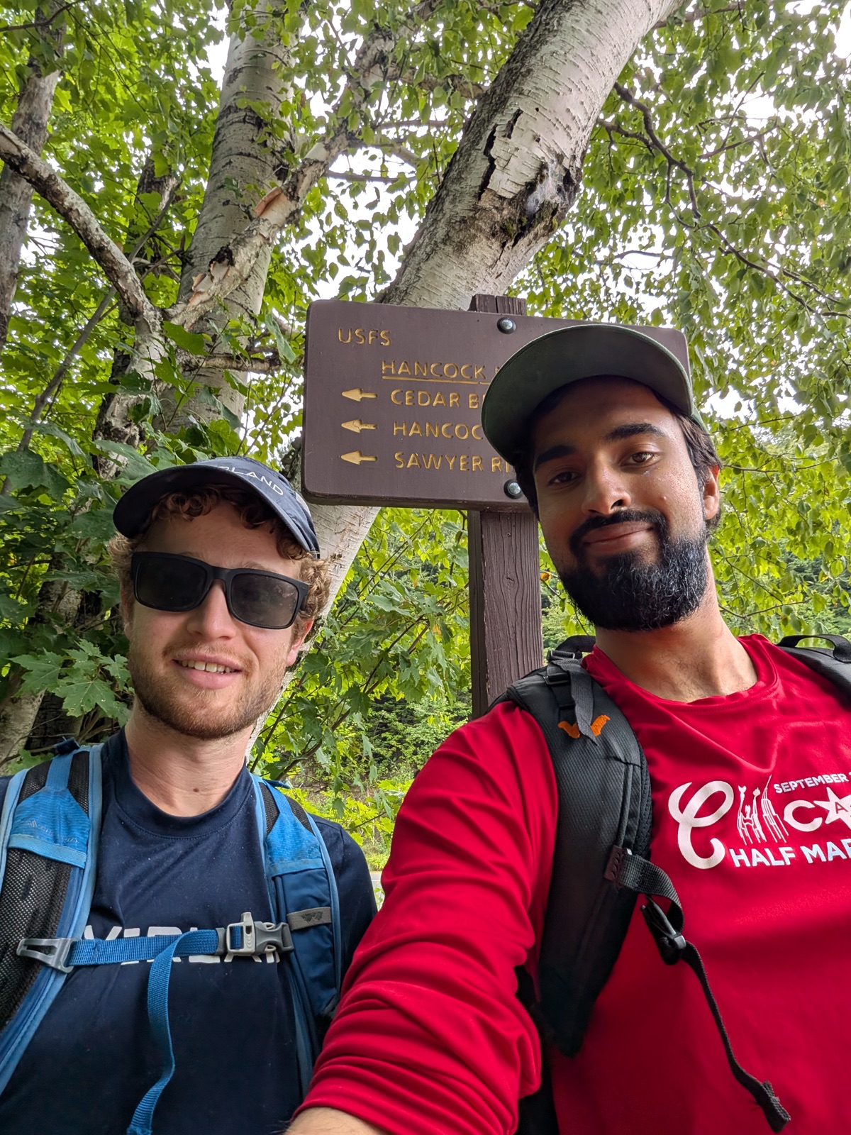 Two hikers taking a selfie at a wooden trail junction sign