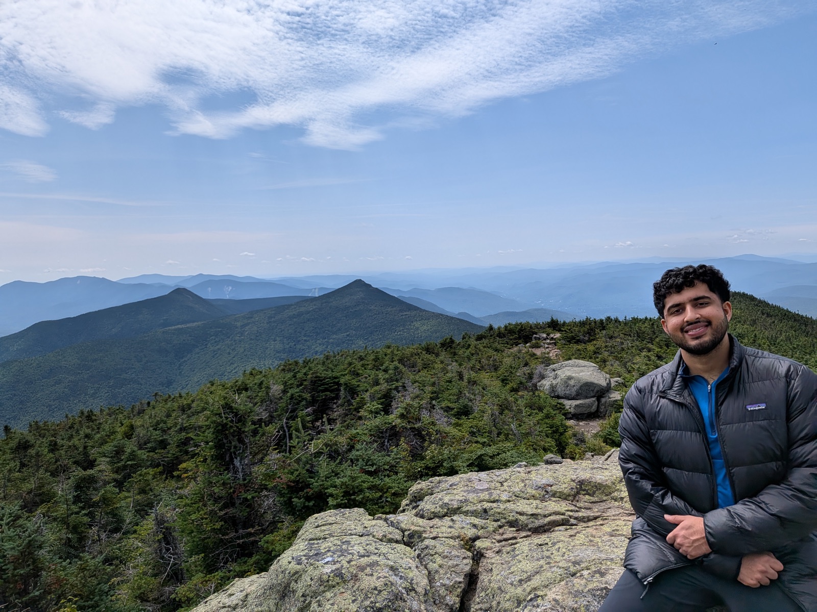 Hiker sitting on a rocky summit with a pointed peak behind