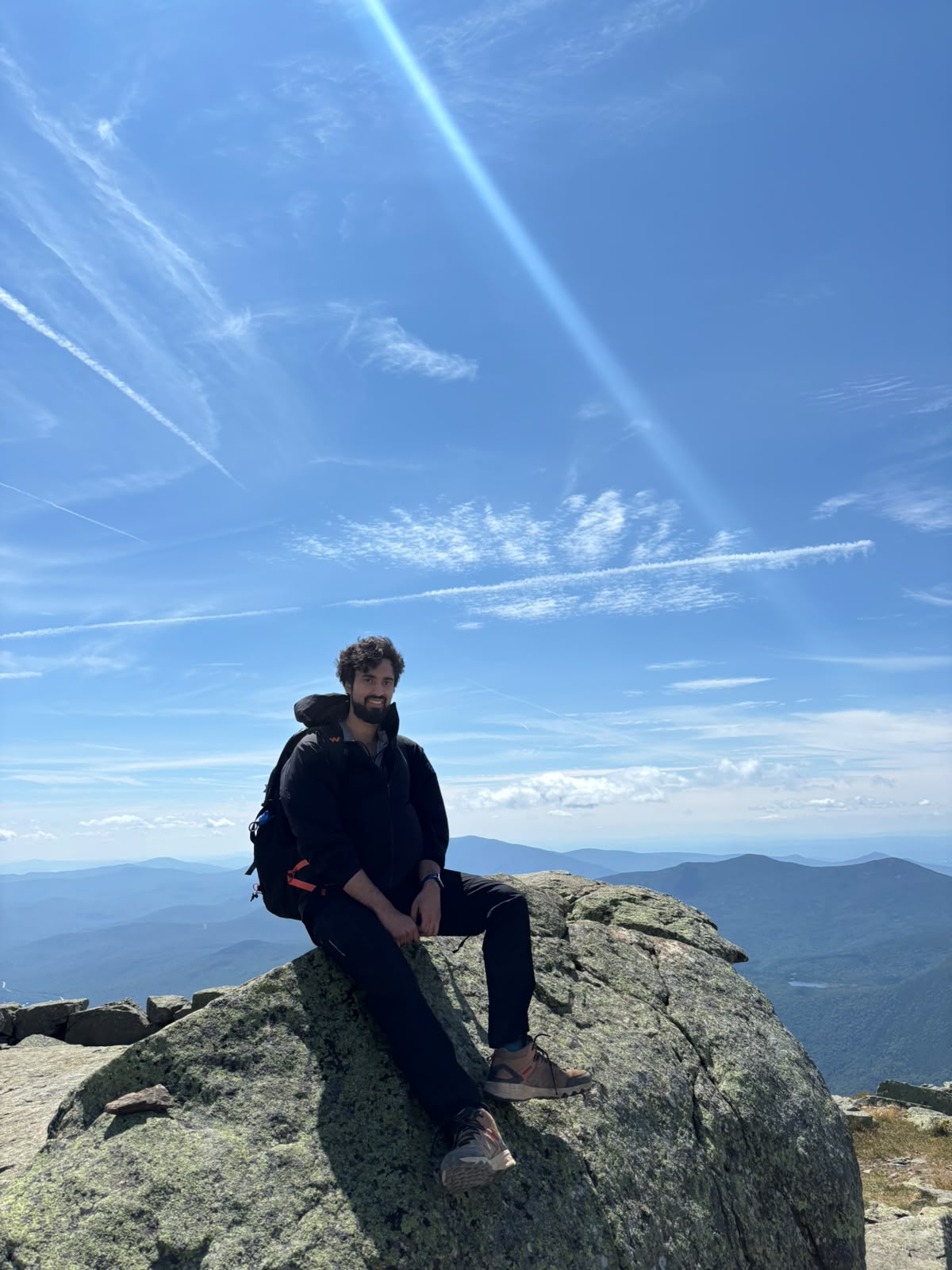 Hiker sitting on a large summit boulder under a deep blue sky