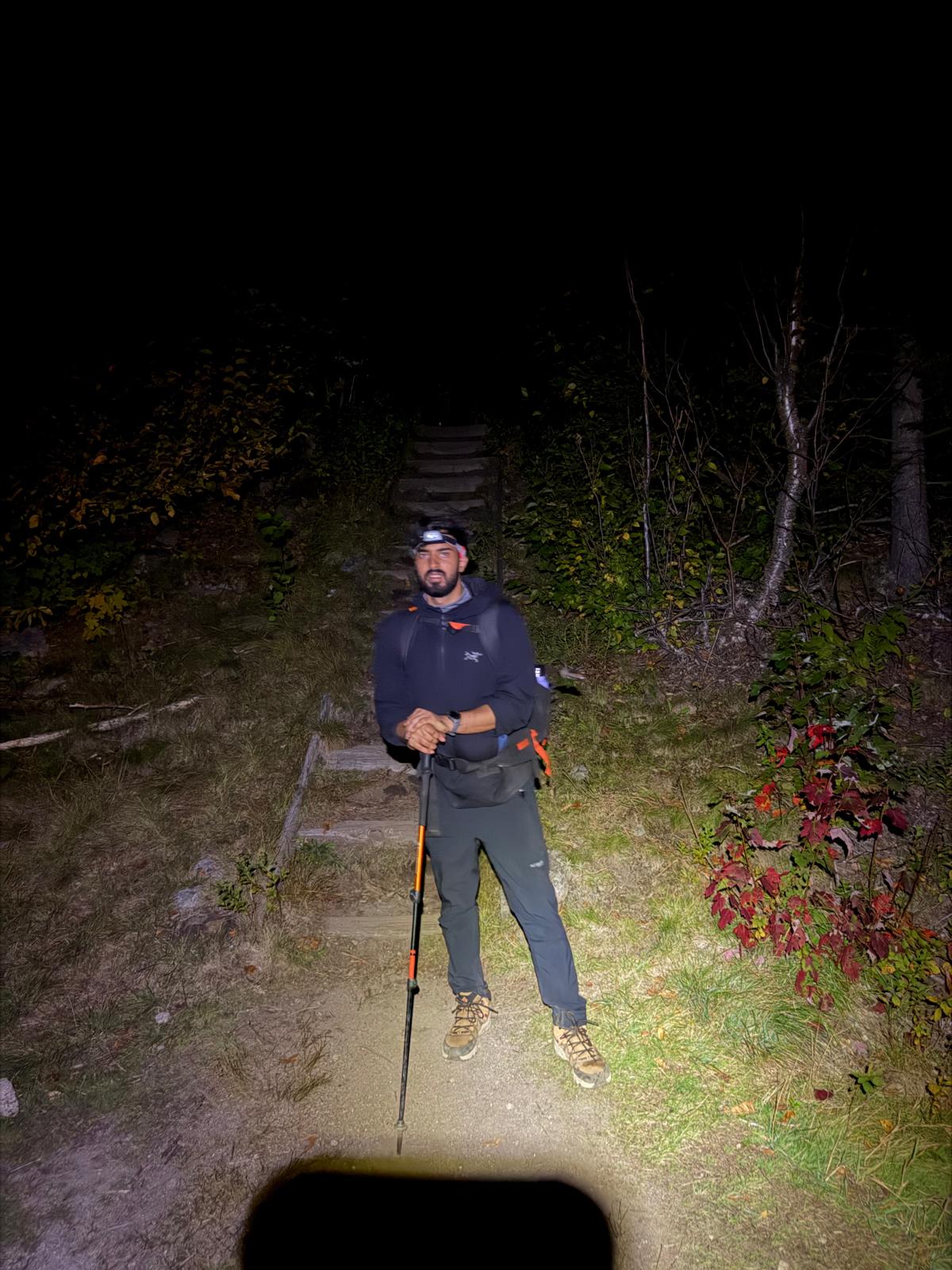 Hiker on a wooded trail at night, lit by headlamp
