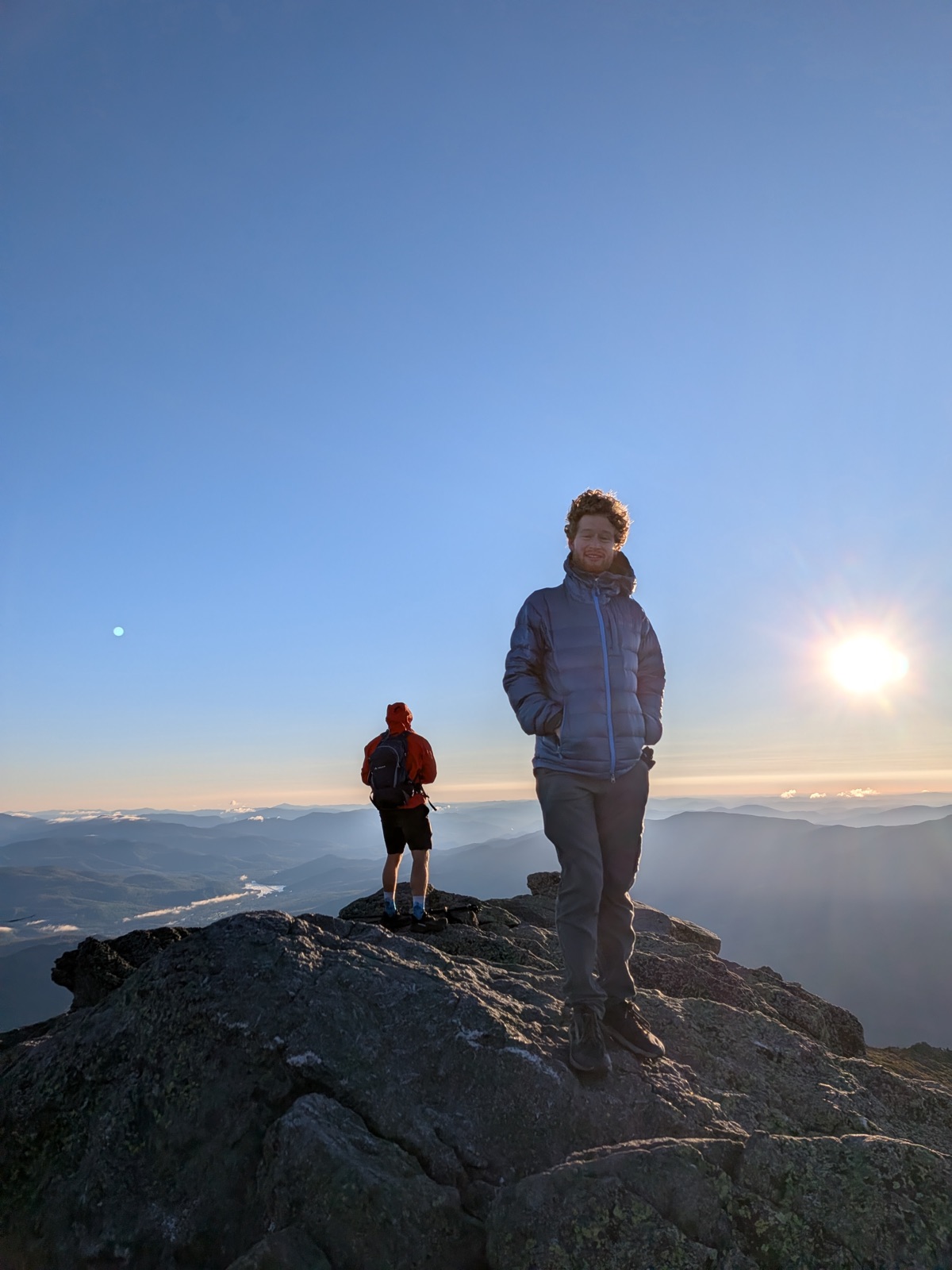 Two hikers on a rocky summit as the sun comes up