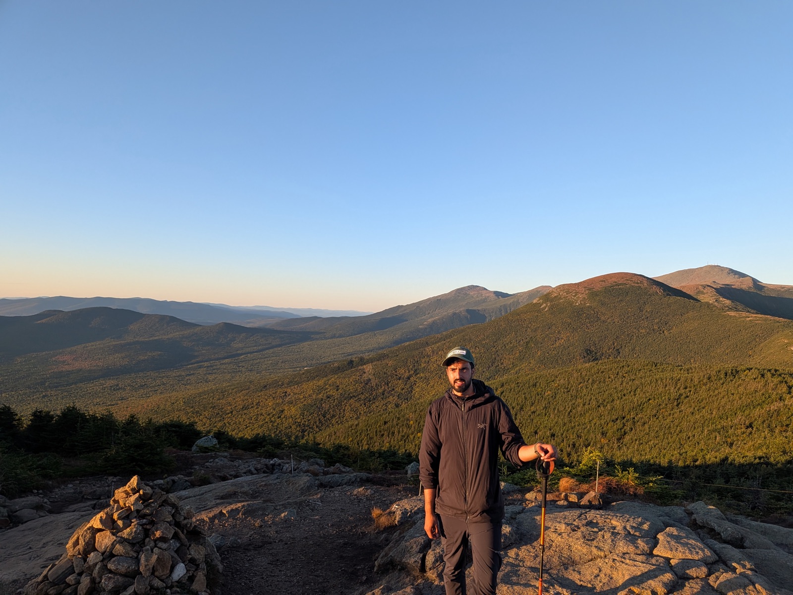 Hiker beside a cairn, forested ridges stretching to the horizon