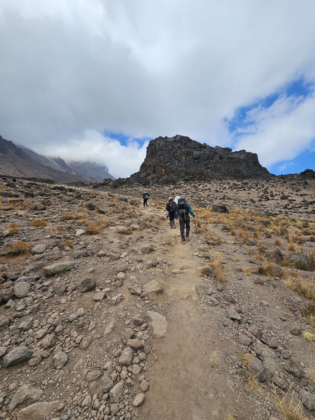 Line of hikers on a rocky trail toward a craggy outcrop