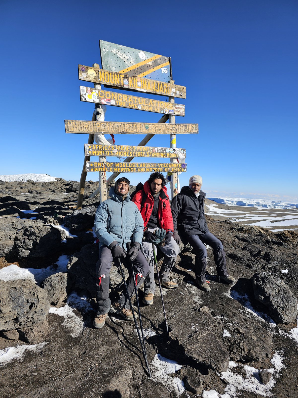 Three hikers resting beneath the summit signpost